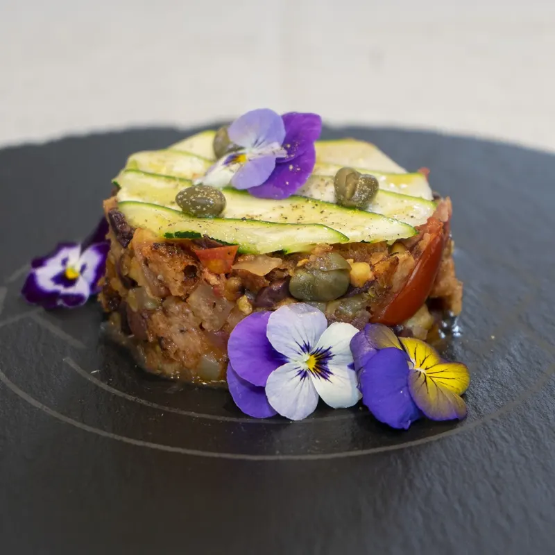 Panzanella-Türmchen mit Zucchinischeiben und essbaren Veilchen auf Schieferplatte