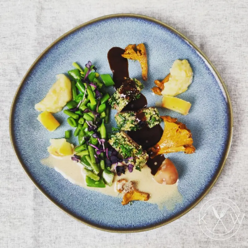 Lamm mit Kräuterkruste, Bohnengemüse und Pfifferlingen auf blauem Teller