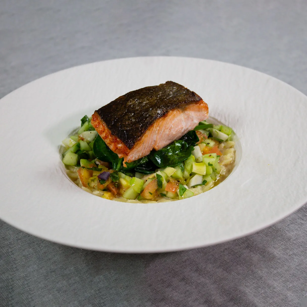 Lachs mit knuspriger Haut auf Spinat und Zitronen-Kritharaki in einem weißen Teller